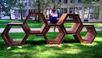 a girl sits on a bench in front of a large hexagonal structure